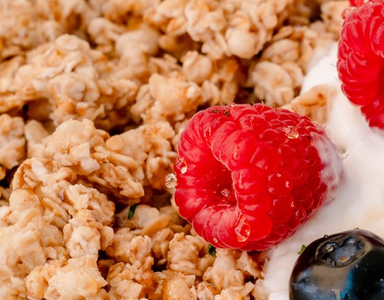 A large bowl of sweet honey-clustered granola served with yoghurt or milk and a side of seasonal fruits.